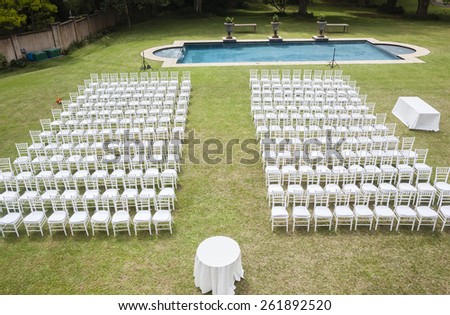 Chairs Wedding Home Outdoors\
White chairs dozens positioned on grass lawn with swimming pool outdoors for private wedding occasion.