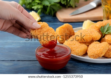 Girl dunks chicken nuggets in ketchup close-up on blue wooden background. fast food