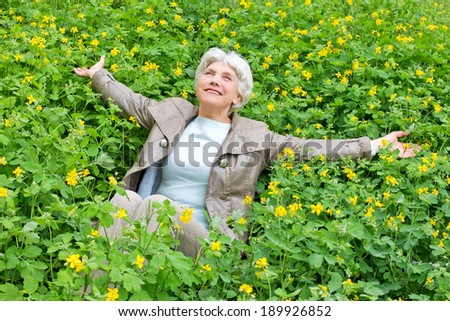 Happy beautiful elderly woman  senior sitting arms outstretched on a glade of yellow flowers in spring