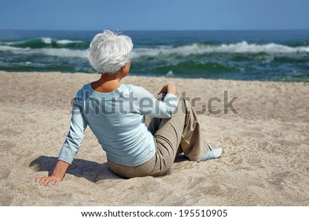 elderly woman sitting in the sand on the beach and looks into the distance the sea horizon