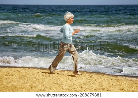elderly happy woman running on the beach along the coast near the sea