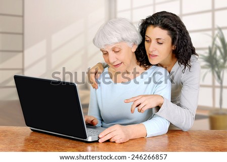 young woman doctrine teaches daughter of an elderly woman how to work using laptop computer at home