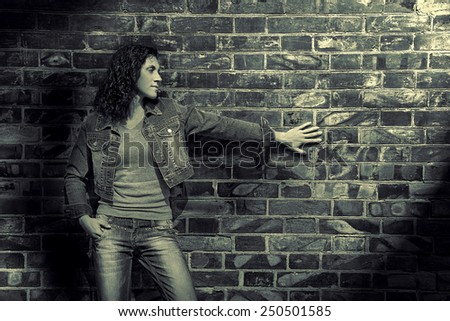 beautiful young woman in jeans and jacket standing on the brick wall background image in the fashion trending monochrome style