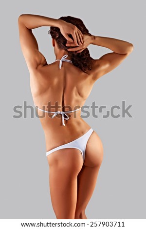 muscular athletic young slim woman in a white bathing suit on a gray background. Fitness. Muscular body. Backs.