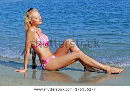Young beautiful blonde woman in pink bikini smiles on the background of the sea