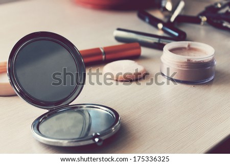Mirror, powder, puff, mascara, eyeliner and other cosmetics on the table
