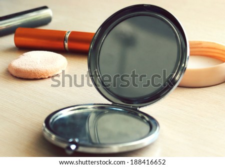 Compact pocket mirror next to a powder puff and other cosmetics