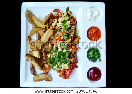 Big white plate with fried potatoes, meat and cheese and sauces isolated on black