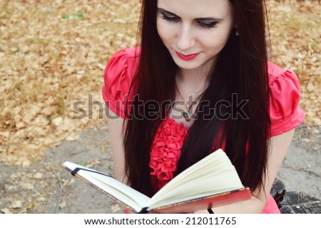 Beautiful brunette woman with long hair reading against autumn nature