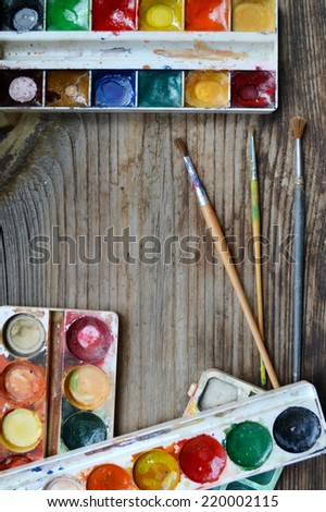 Colorful paints and brushes arranged as a frame on wooden table