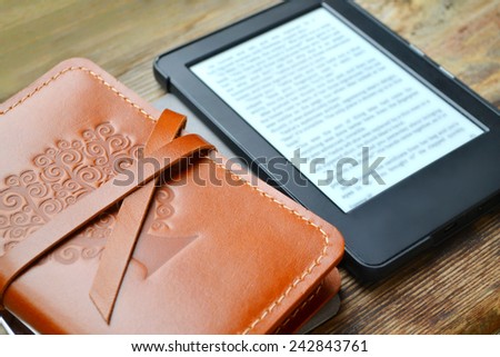 Black ereader with an old notebook in leather cover on wooden table