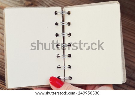 Beautiful woman\'s hand with red nails holding an empty retro spiral notebook with old paper
