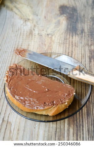 A toast with chocolate spread all over it with a knife on wooden table