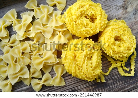 Raw pasta Reginette (Mafaldine) and butterfly shaped pasta farfalle on wooden table