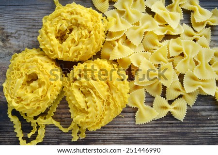 Raw pasta Reginette (Mafaldine) and butterfly shaped pasta farfalle on wooden table