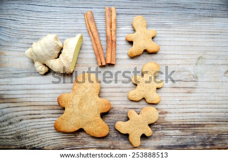Gingerbread cookies in shape of man with cinnamon stick and ginger root on wooden table