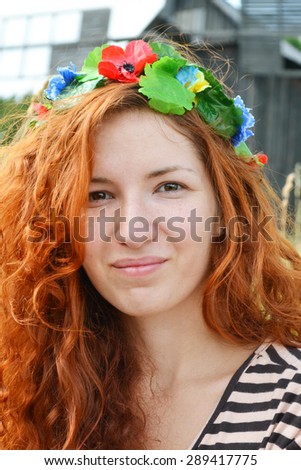 Beautiful young ukrainian redhead woman with flowers in her hair smiling happily with a mill at the background