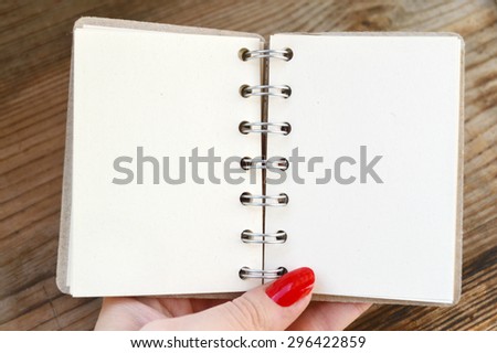 Beautiful woman's hand with red nails holding an empty retro spiral notebook with old paper