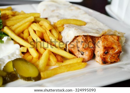 Big white plate with French fries, chicken meat in pitta bread, pickles, salad and sauce