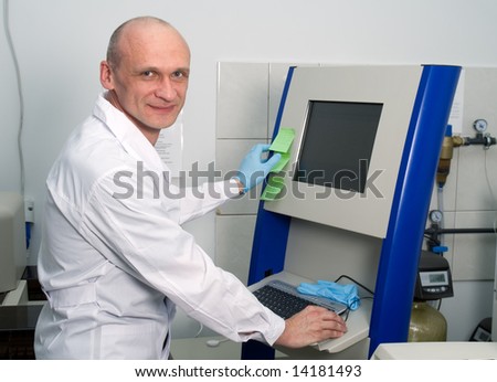 Researcher in white-coat and one blue glove standing in front of monitor