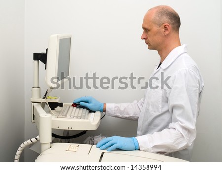 Researcher in white-coat and blue glove standing in front of monitor
