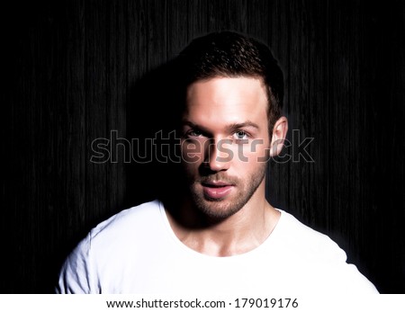 portrait of young good looking man staring at viewer against black background