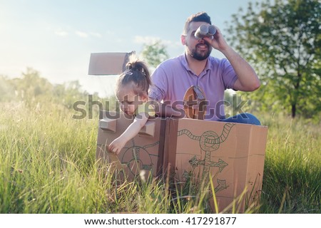 Father and toddler girl playing with paperboard ship in the yard