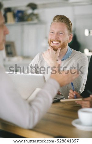 Business people in smart casual wear are discussing affairs, using a laptop, drinking coffee and smiling while co-working in the cafe