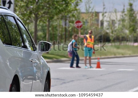 A school crossing guard walks a student across a crosswalk holding a STOP sign