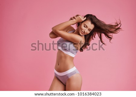 Feeling beautiful.  Attractive young woman in underwear smiling while standing against pink background