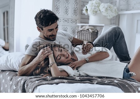 Simple joy of loving. Attractive young people lying on the bed and smiling while spending free time at home