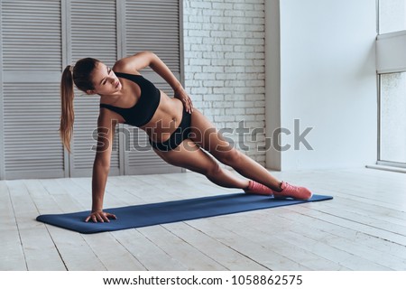 Confident in her fitness regime. Beautiful young woman in sport clothing keeping side plank pose while exercising in the gym