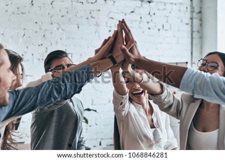 High-five for success! Diverse group of business colleagues giving each other high-five in a symbol of unity and smiling while working in the board room