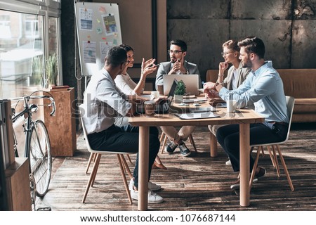 Confident and successful team. Group of young modern people in smart casual wear discussing business while sitting in the creative office
