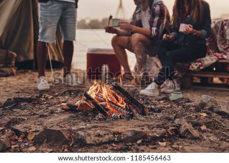 Great warm evening. Close up of young people eating roasted marshmallows while camping near the lake