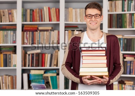 I am ready to my final exam. Cheerful young man holding a book stack and smiling while standing at the library