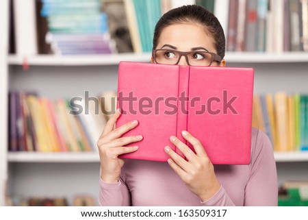 Worried about her exams. Terrified young woman looking out of the book while standing in front of the book shelf