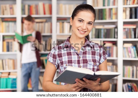 I am ready for my exam. Beautiful young woman holding a book and smiling while man reading on the background
