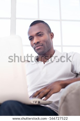 Working at home. Handsome young African man using computer and while sitting on the chair