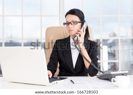 Businesswoman at work. Confident young business woman talking on the phone and using computer while sitting at her working place