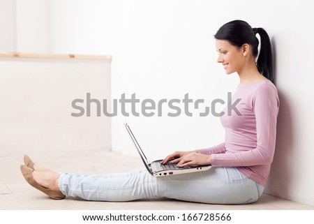 Working at the computer. Beautiful young woman sitting on the floor and using computer