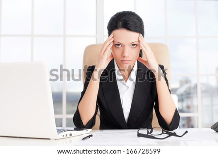 Tired businesswoman. Young business woman holding head in hands and looking at camera while sitting at her working place