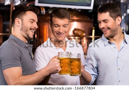 Old friends meeting. Three cheerful young men drinking beer in bar
