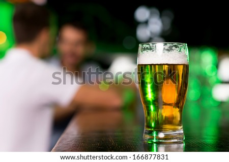 Glass of beer. Close-up of glass with beer on bar with people talking on the background