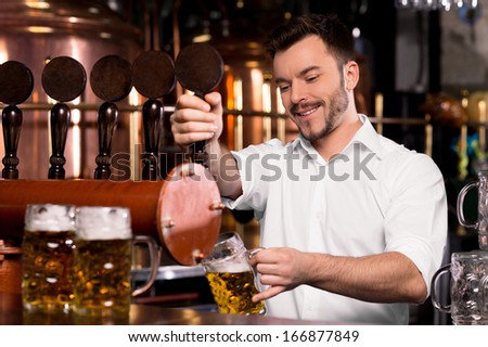 Freshly tapped beer. Cheerful young bartender pouring beer and smiling