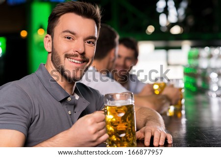 Man in bar. Handsome young man drinking beer in bar and smiling