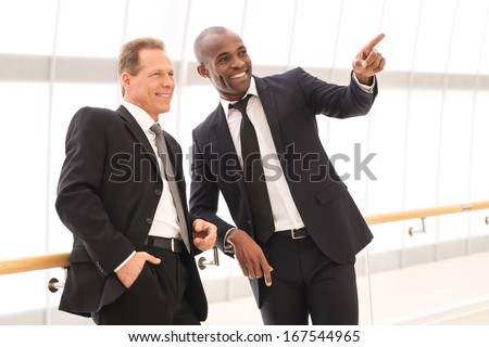 Business people. Two cheerful business men standing close to each other while one of them pointing away and smiling
