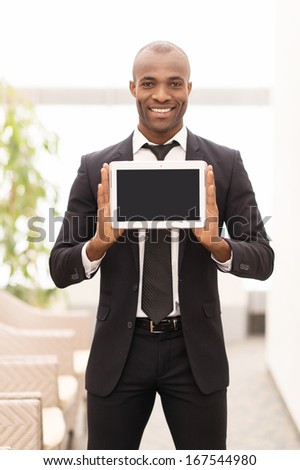 Join A Digital Age. Cheerful Young African Man In Formalwear Showing A Screen Of Digital Tablet And Smiling At Camera
