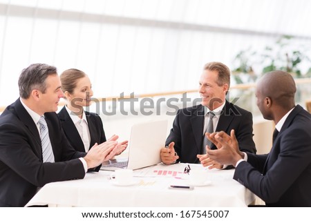 Good job done. Business people in formalwear sitting together at the table and applauding