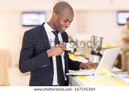 Business on the go. Cheerful young African man in formalwear using his laptop while standing at the bar